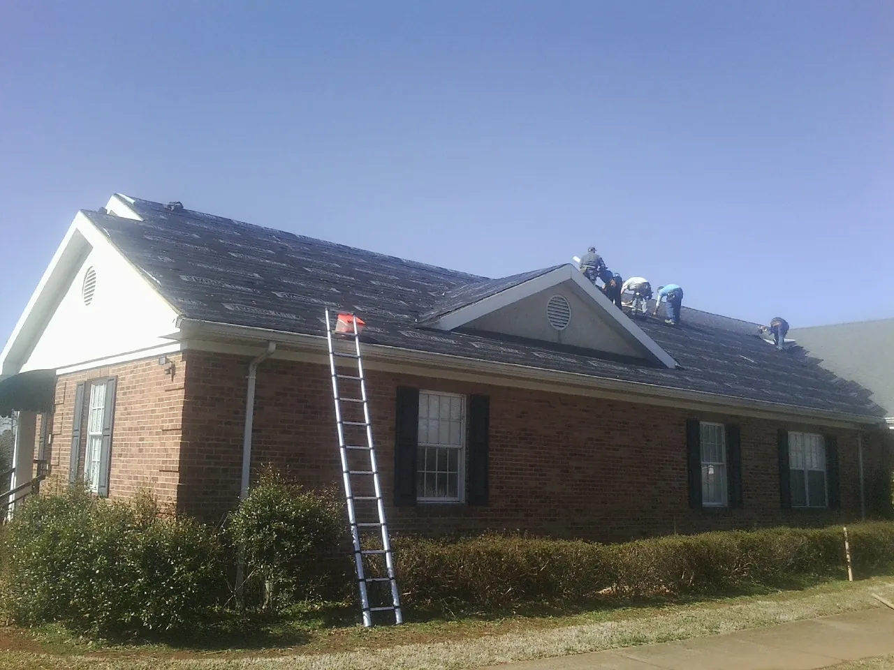 Crew tearing shingles off a brick ranch roof with a ladder set — Metal Roof Repair work by our crew in Jamaica