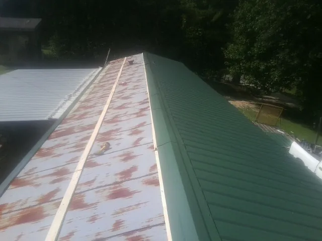 Old rusted panels beside newly installed green metal roofing — Wind Damage Roof Repair by Roofing Brothers in Jamaica
