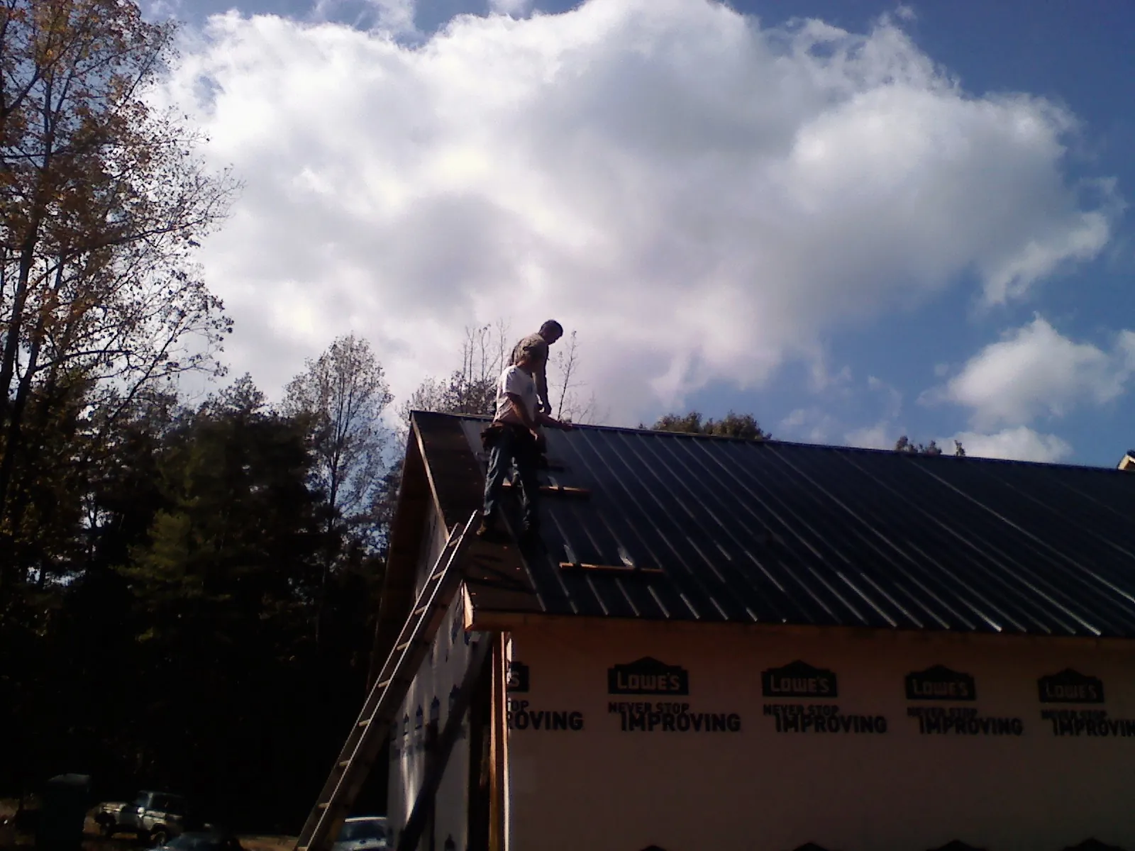 Roofer fastening dark metal panels high against a cloudy sky, from a Roof Inspection job in Jamaica